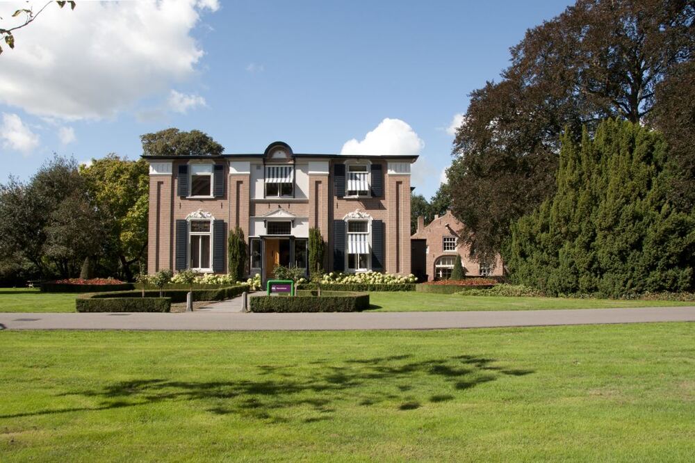 Statig herenhuis met luiken achter een groot gazon met oude bomen in Ermelo